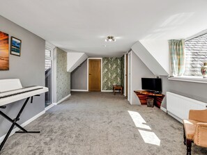 Ein Zimmer mit Klavier, Fernseher und einem fenster mit Vorhängen.