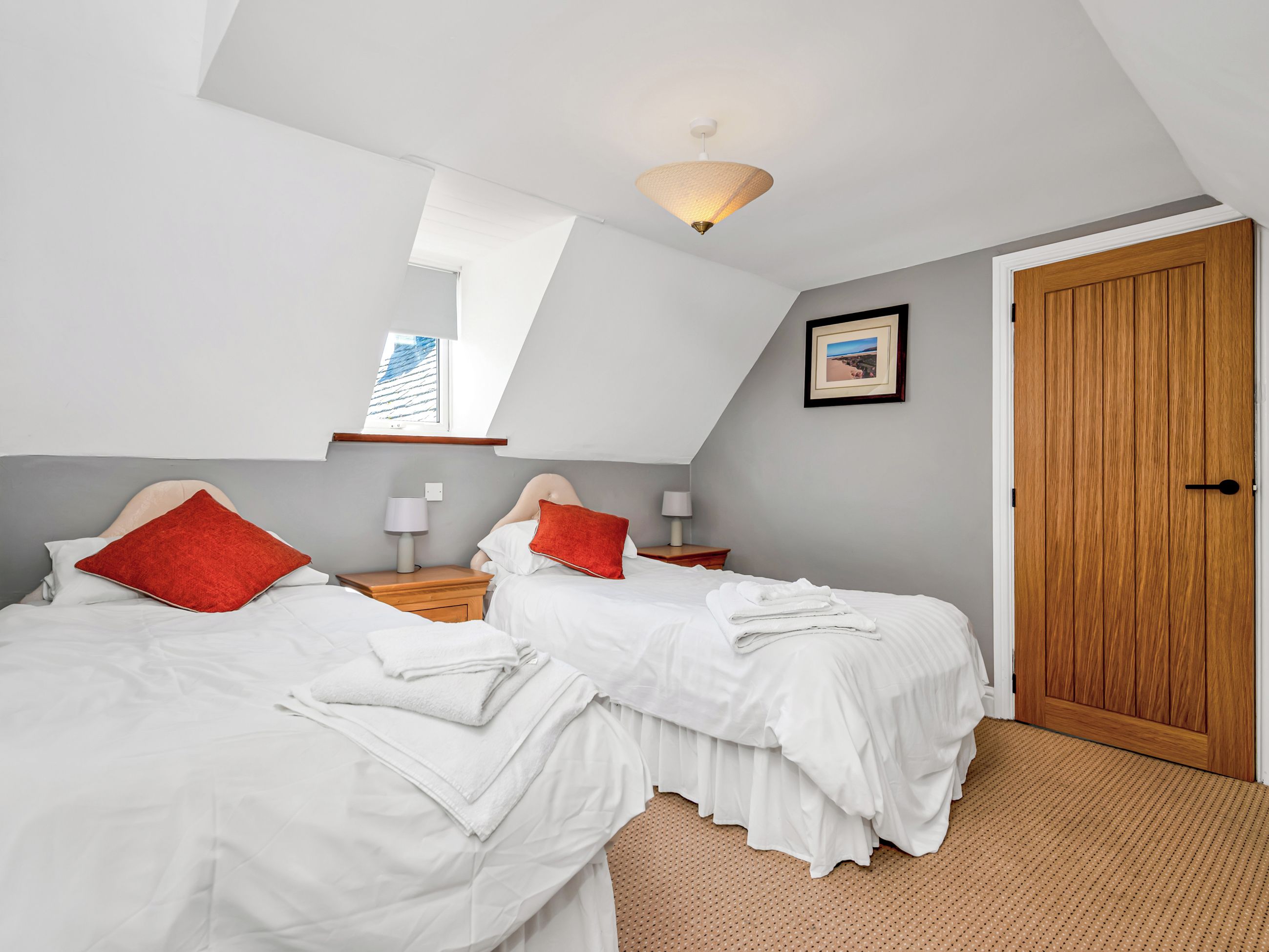 A bedroom with two beds, a wooden door, a window, and a ceiling light fixture.