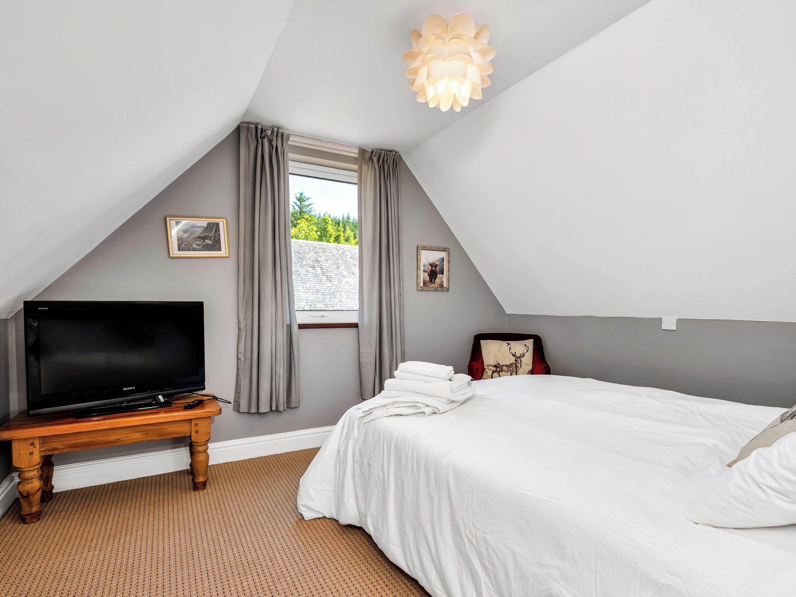 A bedroom with a bed, a television on a wooden table, a window with curtains, and a ceiling light fixture.