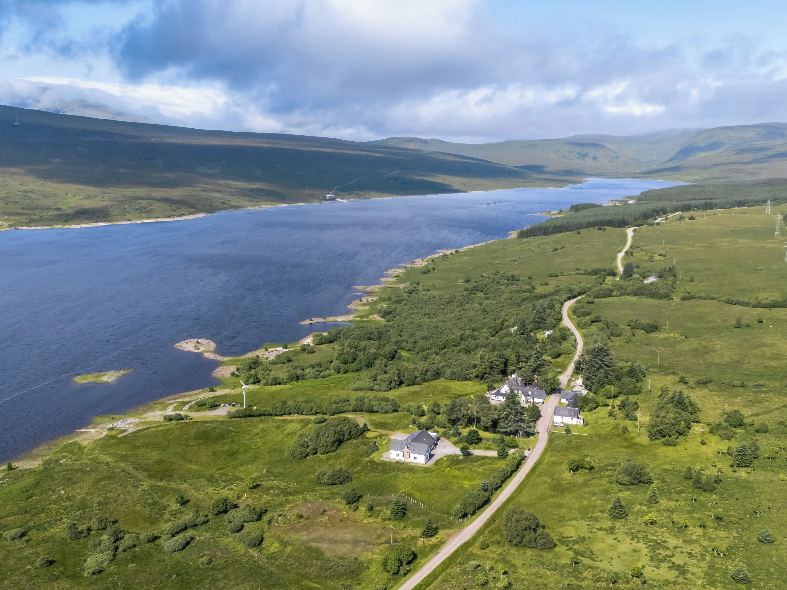 Un paysage côtier avec une route sinueuse, un petit groupe de maisons et une vaste étendue d’eau.