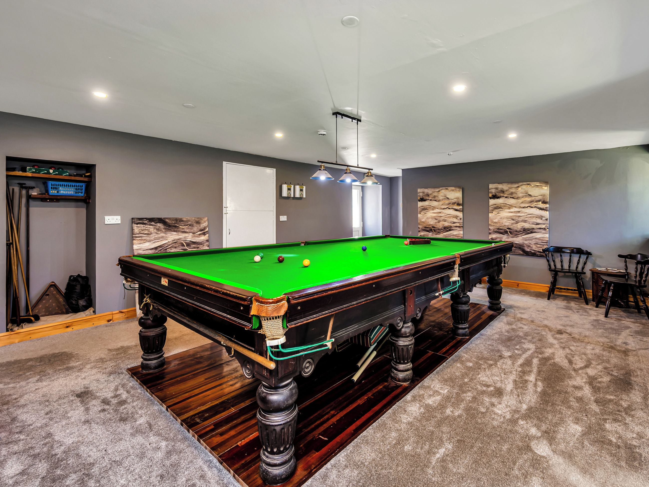Une table de billard dans une pièce avec un mur gris, une porte et un tableau.
