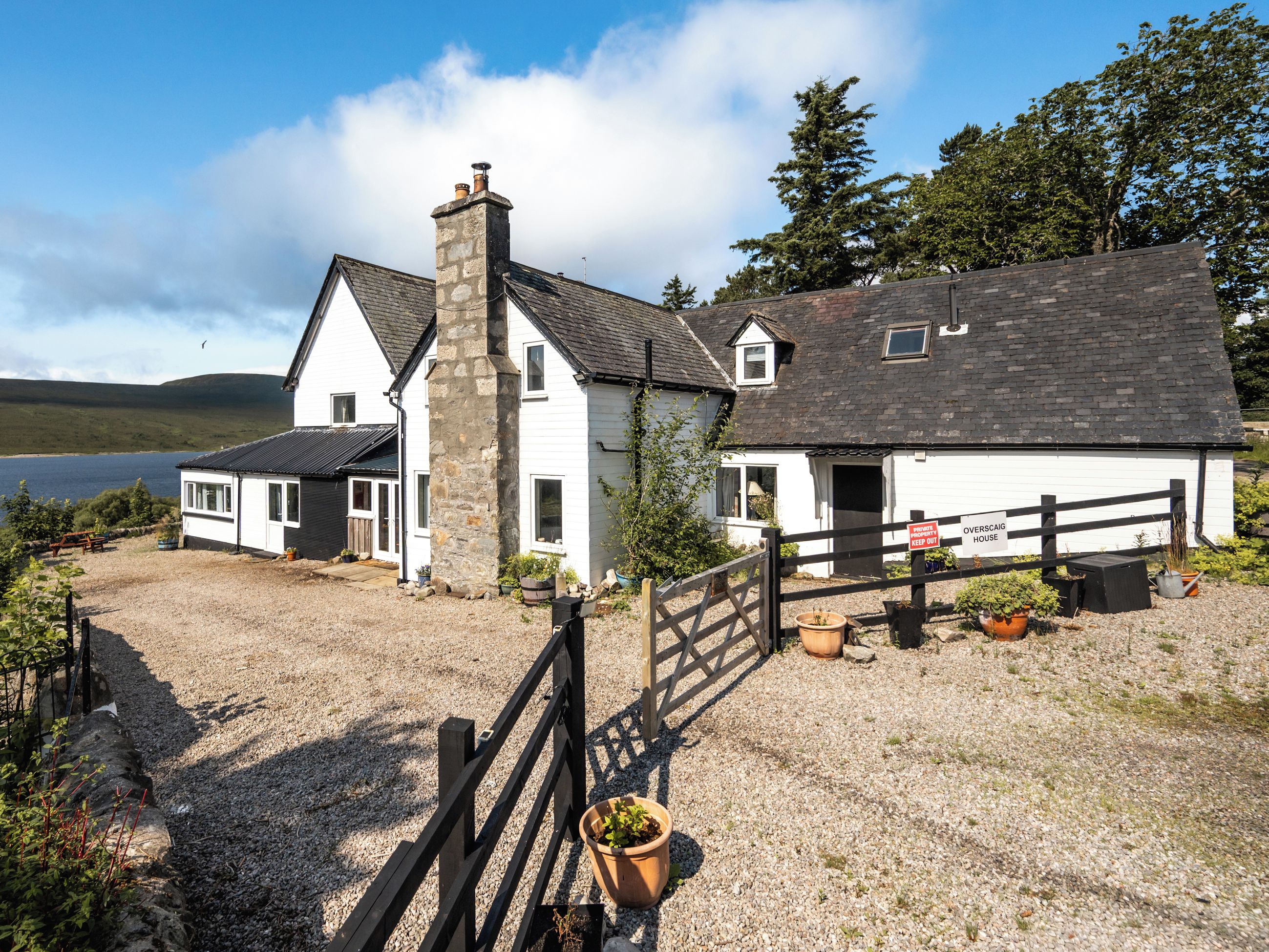 A white house with a stone chimney, a gravel driveway, and a wooden fence.