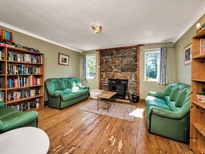 A cozy living room with a stone fireplace, green leather sofas, a wooden bookshelf, and a white ceiling. - Overscaig House - UK51360 (Lairg)
