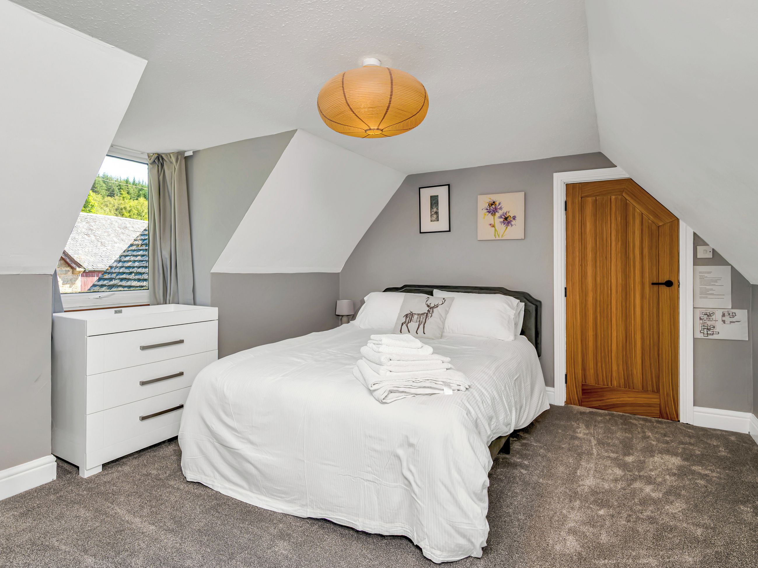 Une chambre à coucher avec un lit, une commode, une fenêtre, une porte et un luminaire au plafond.