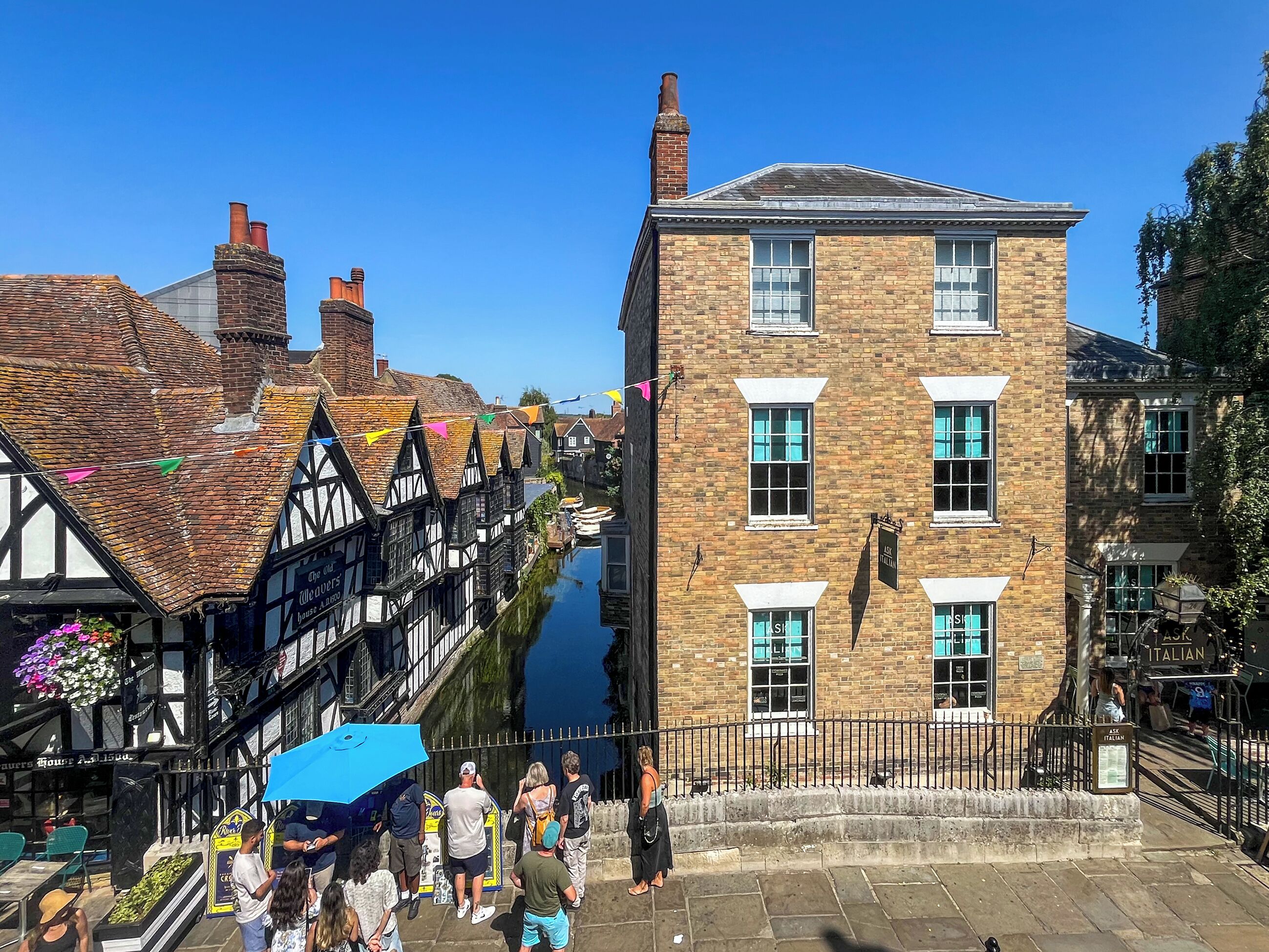 Een smalle straat met historische gebouwen, een gracht en mensen die wandelen.