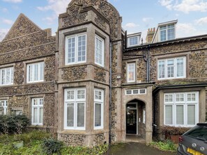 A stone building with multiple windows and a door, surrounded by greenery.