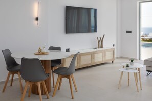 Ein moderner Essbereich mit einem runden Tisch, grauen Stühlen, einem Holzschrank und einem Fernseher an der Wand.