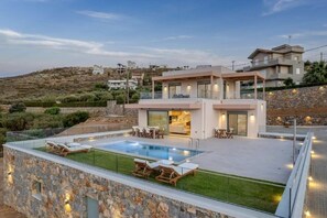 Ein modernes Haus mit Swimmingpool, Sitzgelegenheit im Freien und einer Steinmauer.