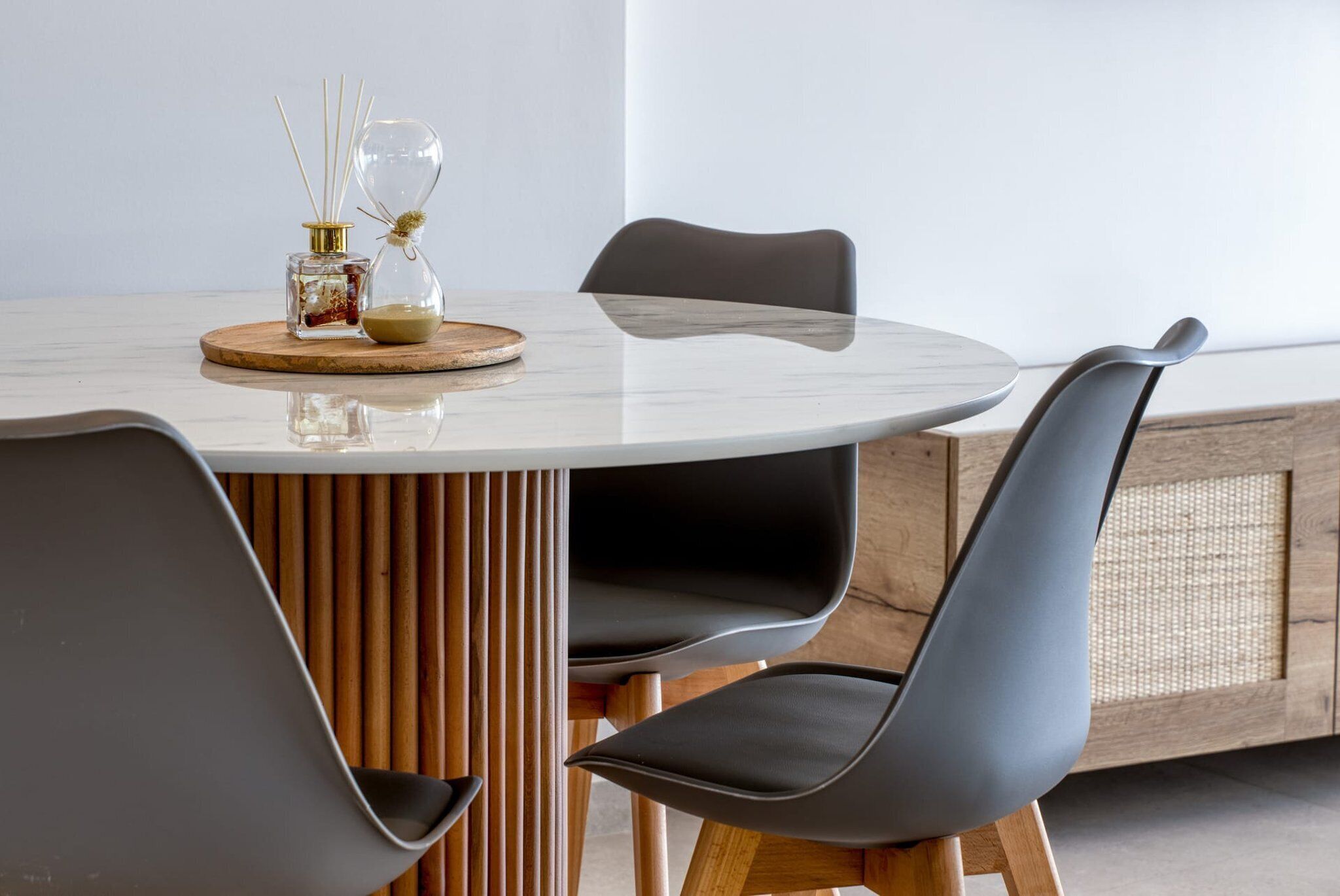 A round table with a marble top, surrounded by four black chairs with wooden legs. There is a small wooden board with a glass jar and reed diffuser on the table.