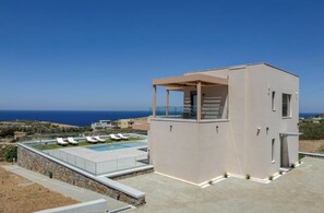 Eine moderne Villa mit Pool, Liegestühlen und Meerblick.