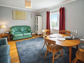 A room with a green sofa, wooden dining table, and chairs, a cabinet, and a window with curtains.