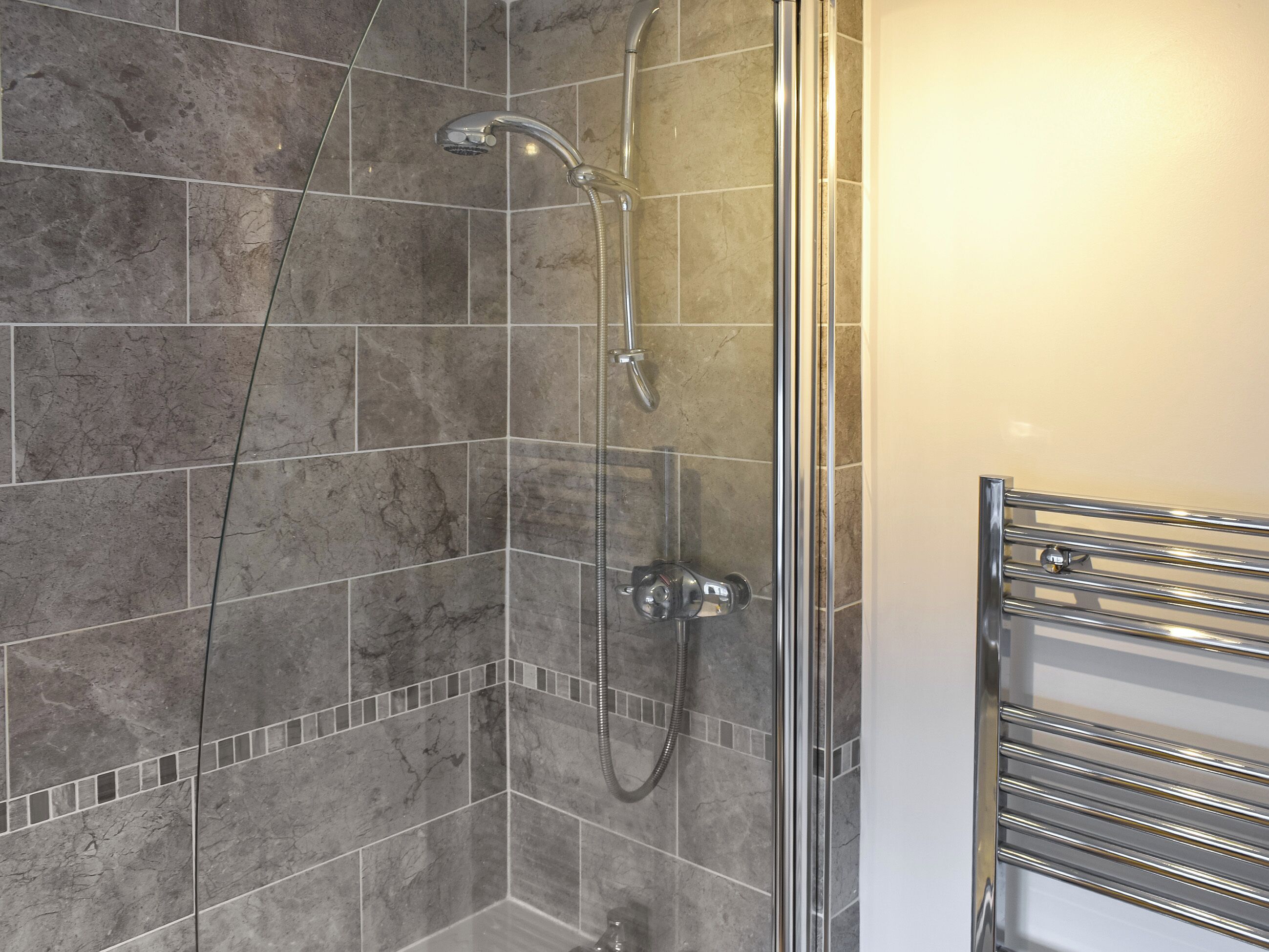 A shower area with a glass door, a chrome showerhead, and a chrome towel rack.