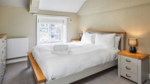 Un dormitorio con cama, mesitas de noche, un radiador y una ventana con vista a coches estacionados.