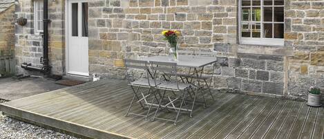 A stone building with a wooden deck, a table with chairs, and a potted plant.