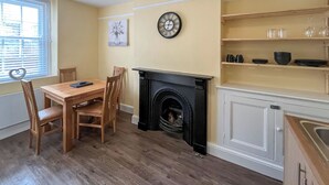 Un comedor con una mesa y sillas de madera, una chimenea, un reloj y una ventana con persianas.