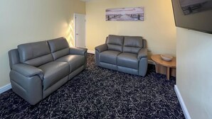 Una sala de estar con dos sofás grises, una alfombra estampada, un cuadro en la pared y una pequeña mesa de madera con un cuenco.