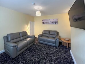 Ein Wohnzimmer mit zwei grauen Sofas, einem gemusterten Teppich, einem Bild an der Wand und einem kleinen Holztisch mit einer Schale.