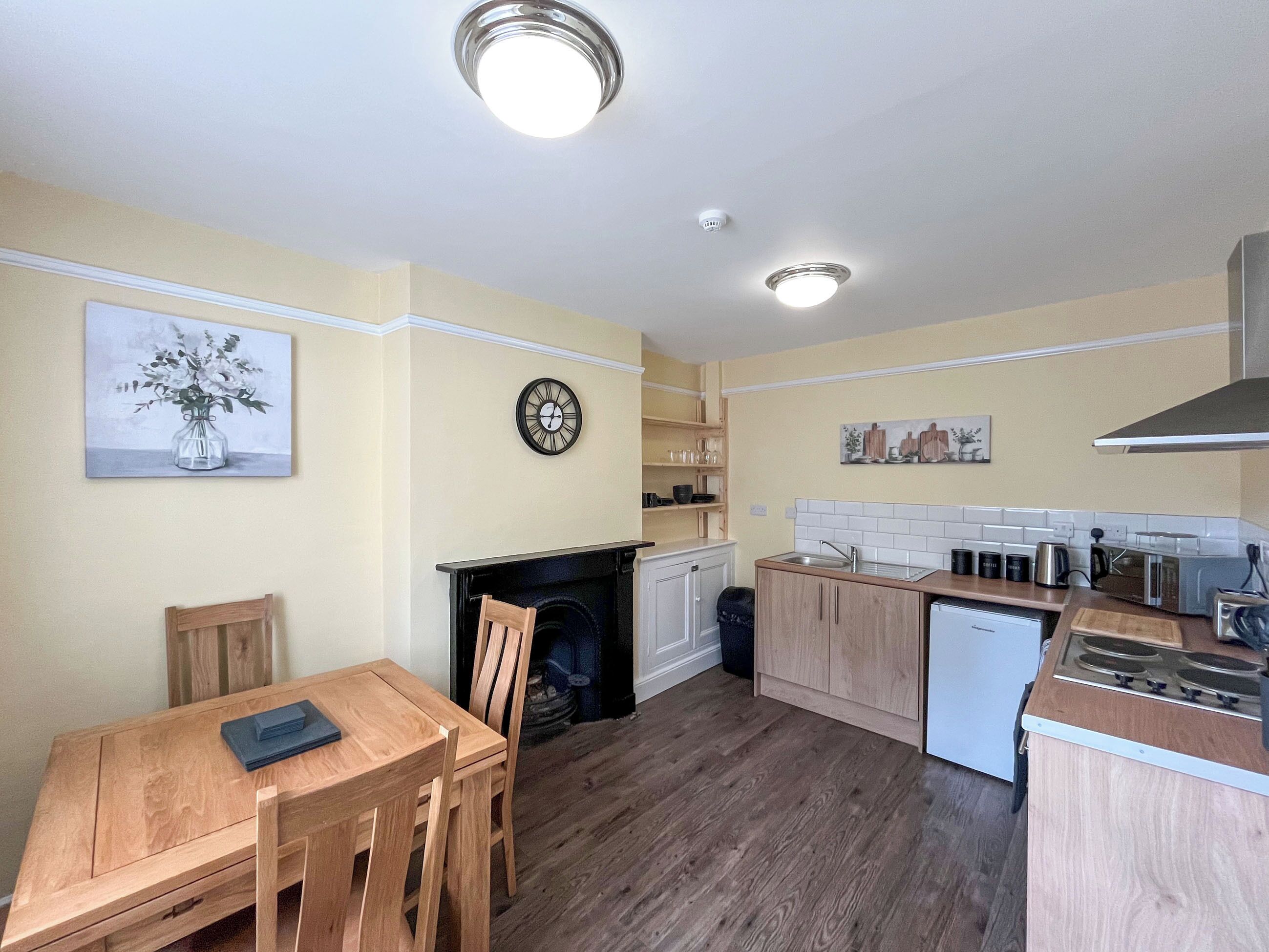 A compact kitchen with wooden cabinets, a built-in oven, a microwave, and a sink. There is a dining table with chairs and a painting on the wall.