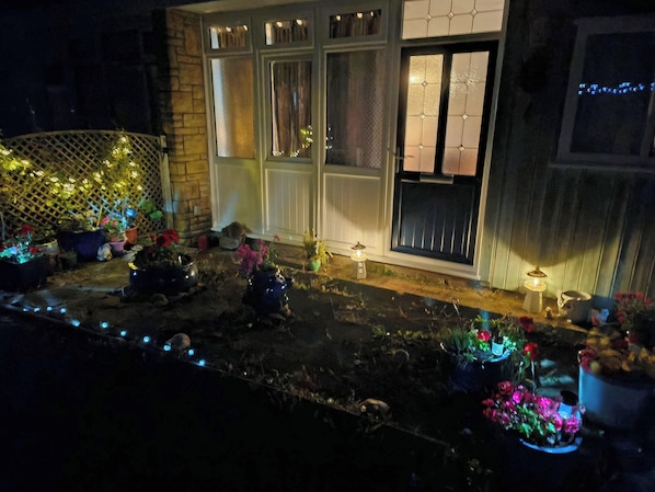 Une maison dotée d’un porche à l’avant, décoré de plantes en pot et de guirlandes lumineuses.