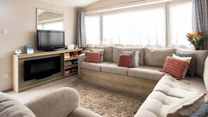Uma sala de estar aconchegante com um sofá, uma TV de tela plana, uma estante de livros e uma janela com cortinas.