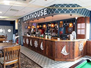 Een bar met een houten toonbank, decoratie met nautische thema en diverse flessen en glazen.