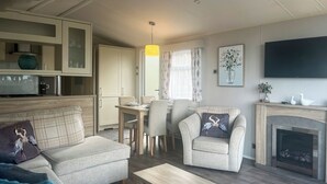 En moderne stue med sofa, lænestole, et sofabord, en pejs og et spiseområde med bord og stole.