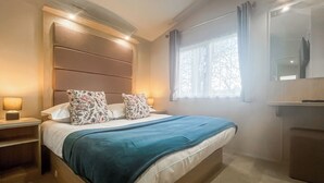 En pænt redt seng med et blåt tæppe, to blomstrede puder og en sengegavl med indbygget belysning.