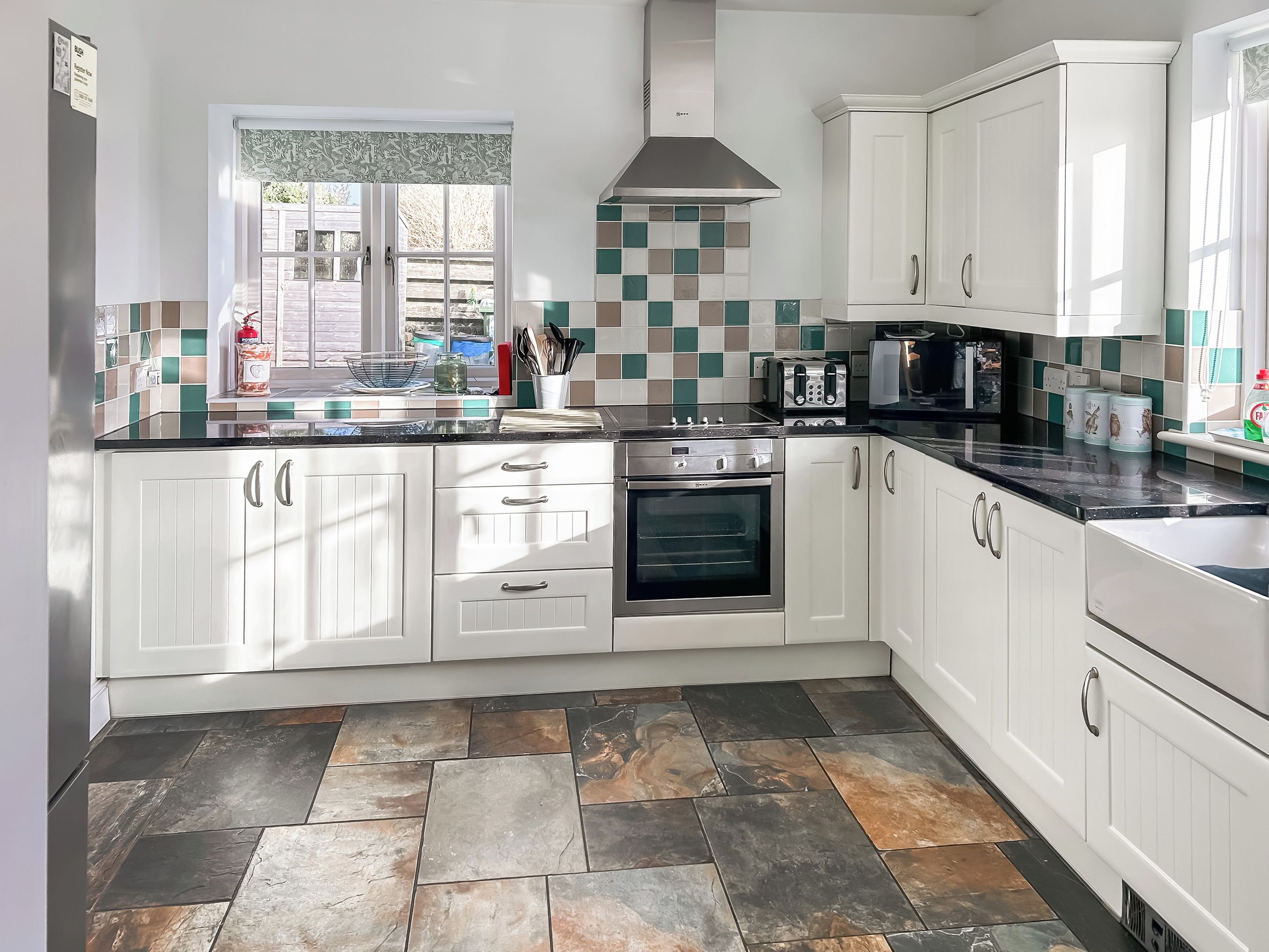 A modern kitchen with white cabinets, a black countertop, a stainless steel range hood, and a tiled backsplash.