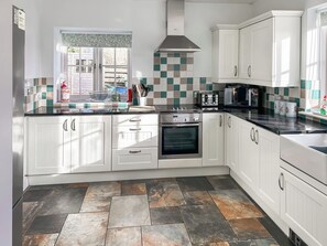 A modern kitchen with white cabinets, a black countertop, a stainless steel range hood, and a tiled backsplash. - 3 bedroom accommodation in Helston (Helston)