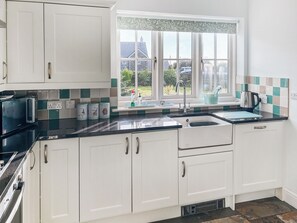 A kitchen with white cabinets, a black countertop, a window with a view of greenery, and a kettle on the counter. - 3 bedroom accommodation in Helston (Helston)
