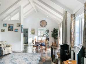 A spacious living room with a high ceiling, a fireplace, a dining area with a wooden table and chairs, and a kitchen visible through an open door. - 3 bedroom accommodation in Helston (Helston)