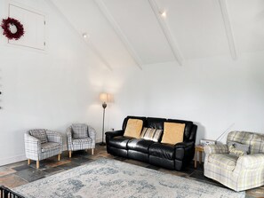 A living room with a black leather sofa, two plaid armchairs, a floor lamp, and a patterned rug. - 3 bedroom accommodation in Helston (Helston)