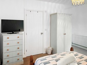 A bedroom with a bed, a dresser with drawers, a television on top, a wardrobe, and a radiator. - 3 bedroom accommodation in Helston (Helston)