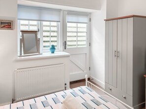 A bedroom with a bed, a radiator, a window with a view, a wardrobe, and a small table with a vase. - 3 bedroom accommodation in Helston (Helston)