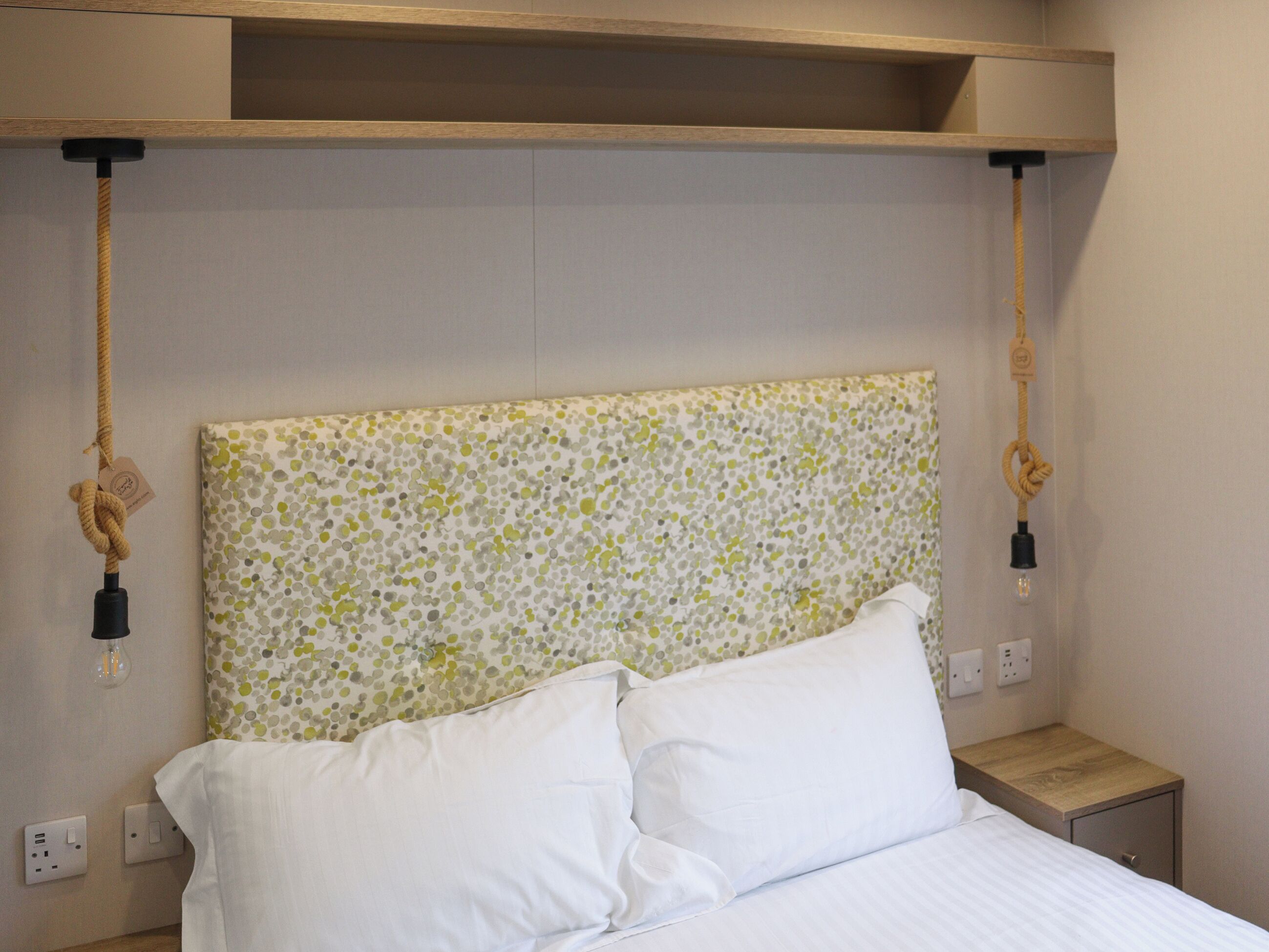 A bed with white bedding, a polka dot headboard, and a wooden nightstand.