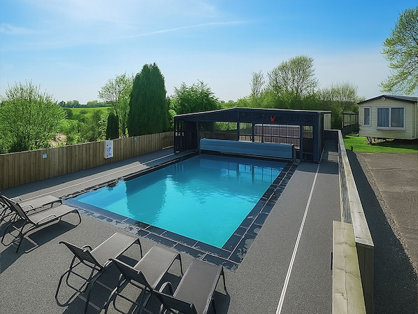 Une piscine dotée d’un espace couvert, de chaises longues et d’une clôture en bois.