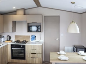 Une cuisine moderne équipée d’un four à micro-ondes, d’un four traditionnel et d’une cuisinière à gaz. On y trouve une table à manger avec des assiettes et des tasses.
