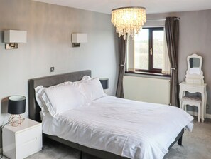 A bedroom with a bed, bedside lamps, a dresser, a mirror, a window with curtains, and a chandelier. - Ty Redford - UK51389 (Narberth)