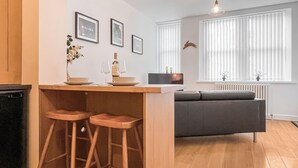 Une cuisine moderne avec des tabourets en bois, une table à manger et un canapé gris dans l’espace salon.