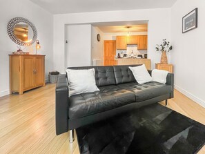 A modern living room with a black leather sofa, wooden cabinets, and a kitchen in the background. - Old Steamship Quarters (Whitby)