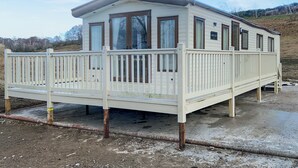 A single-story mobile home with a deck, large windows, and a sign indicating 'ABLESICKE.' - Ballagan Lodge 2 - UK51397 (Inverness)