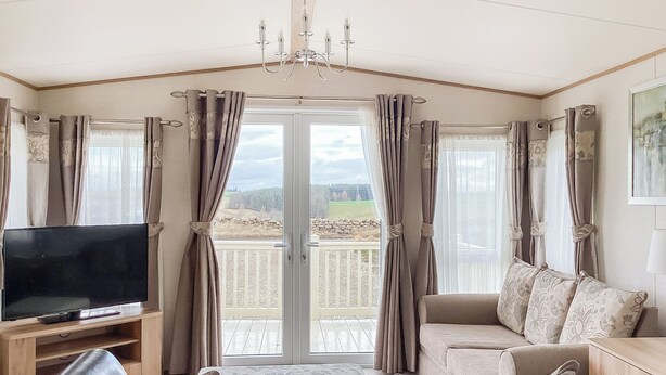 A living room with a television, sofa, and a view of a balcony. - Ballagan Lodge 2 - UK51397 (Inverness)