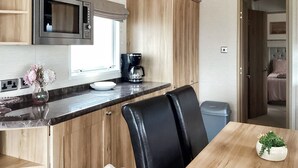 A compact kitchen with a microwave, coffee maker, and a dining area with chairs and a table. - Ballagan Lodge 2 - UK51397 (Inverness)