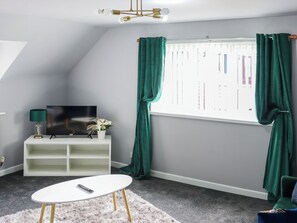 A room with a TV on a white stand, a small white table, a fluffy rug, and green curtains. - 2 bedroom accommodation in Narberth (Narberth)