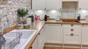A kitchen with white cabinets, a stone wall, a clock, a kettle, and a coffee maker. - 1 bedroom accommodation in South Barrow, near Yeovil (Yeovil)