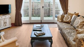 A living room with a sofa, a coffee table, a television on a cabinet, and a sliding glass door leading to a backyard. - 1 bedroom accommodation in South Barrow, near Yeovil (Yeovil)
