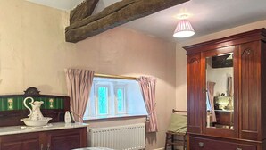 Un dormitorio con cama, cómoda, espejo, radiador y ventana con cortinas.