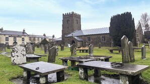Un cementerio con lápidas de piedra y un edificio histórico con una torre al fondo.