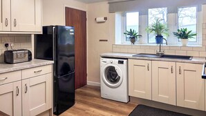 Una cocina moderna con armarios de colores claros, un refrigerador negro, una lavadora y una ventana con plantas en macetas.