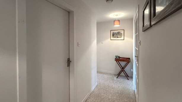 En smal hall med ett mönstrat mattgolv, ett litet träbord och en inramad tavla på väggen.